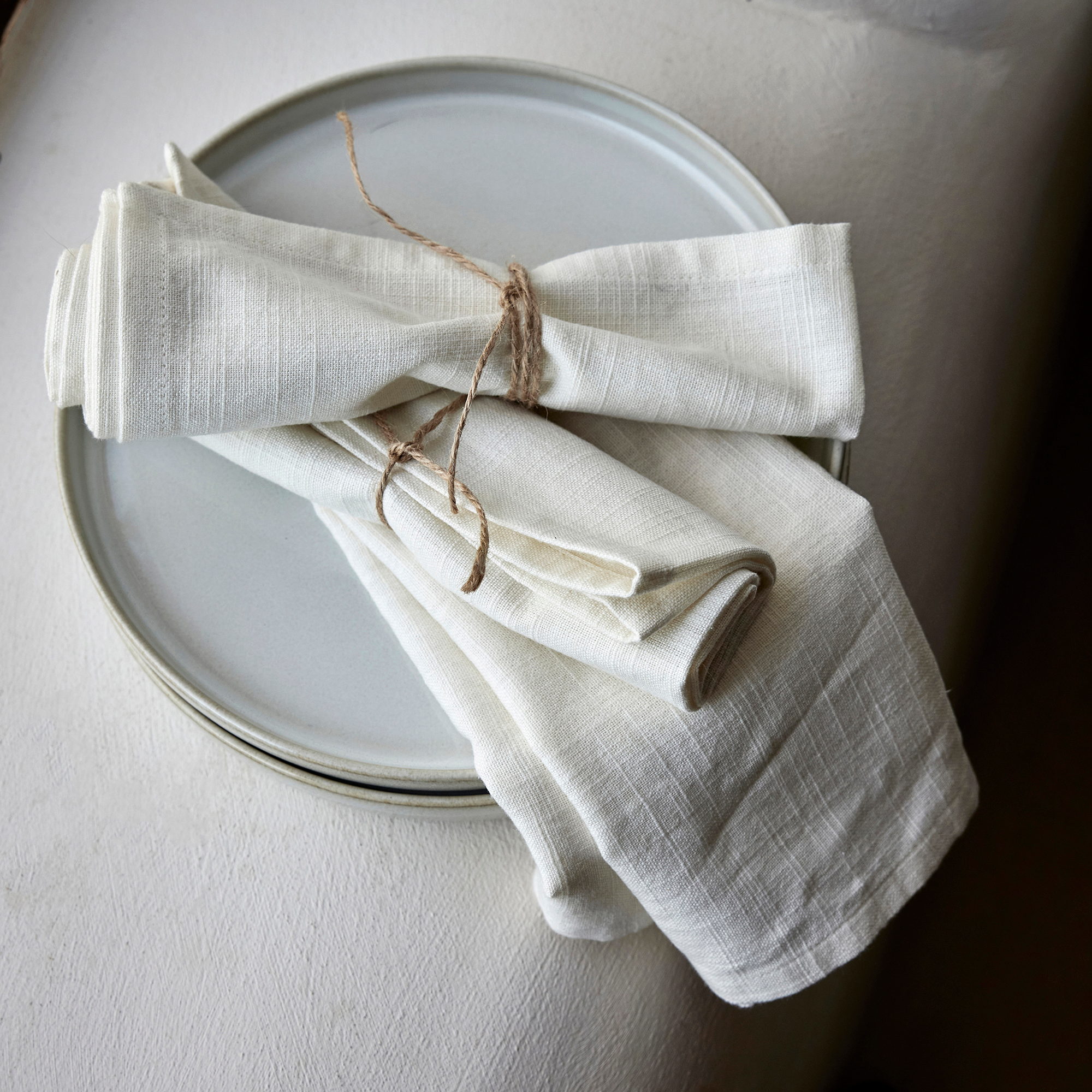 Serviettes en lin nouées d'une ficelle posées sur des assiettes en grès blanc