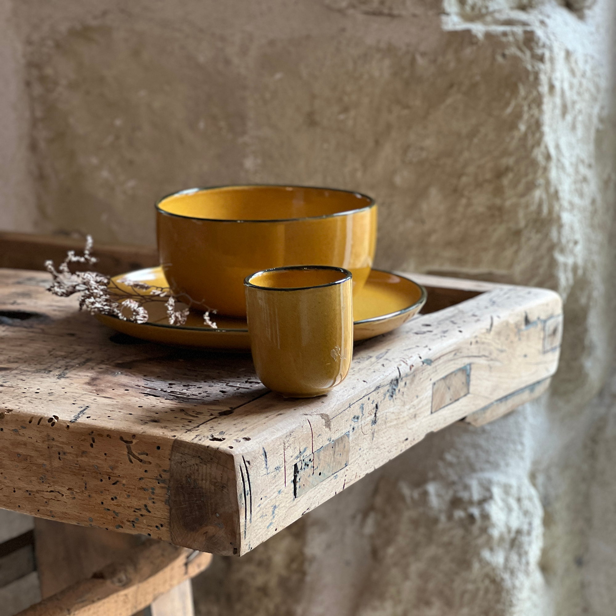 Bols et tasse jaunes sur une planche de bois brut devant un mur de pierre