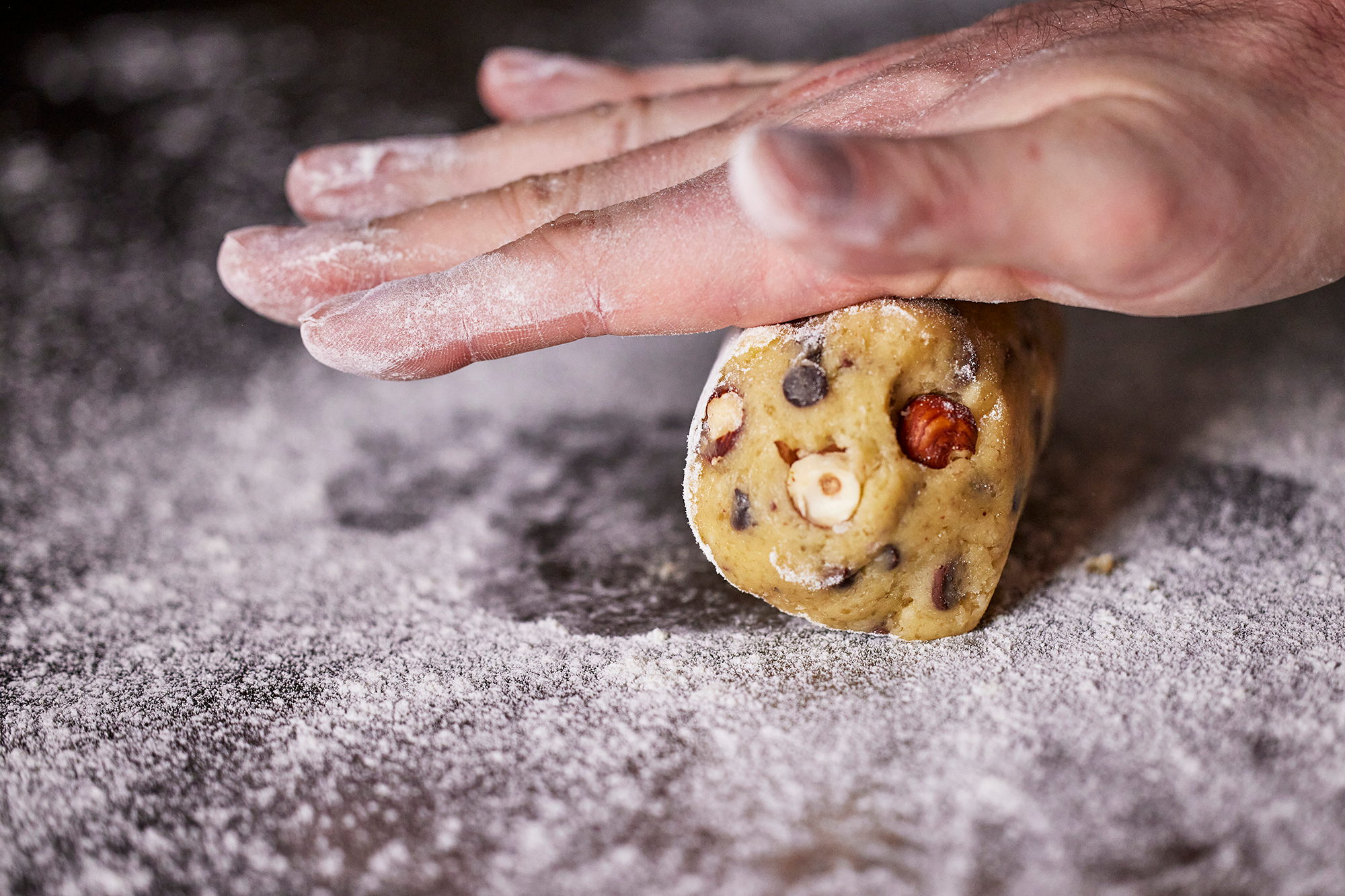 Main écrasant une boule de pâte aux pépites de chocolat sur un plan fariné