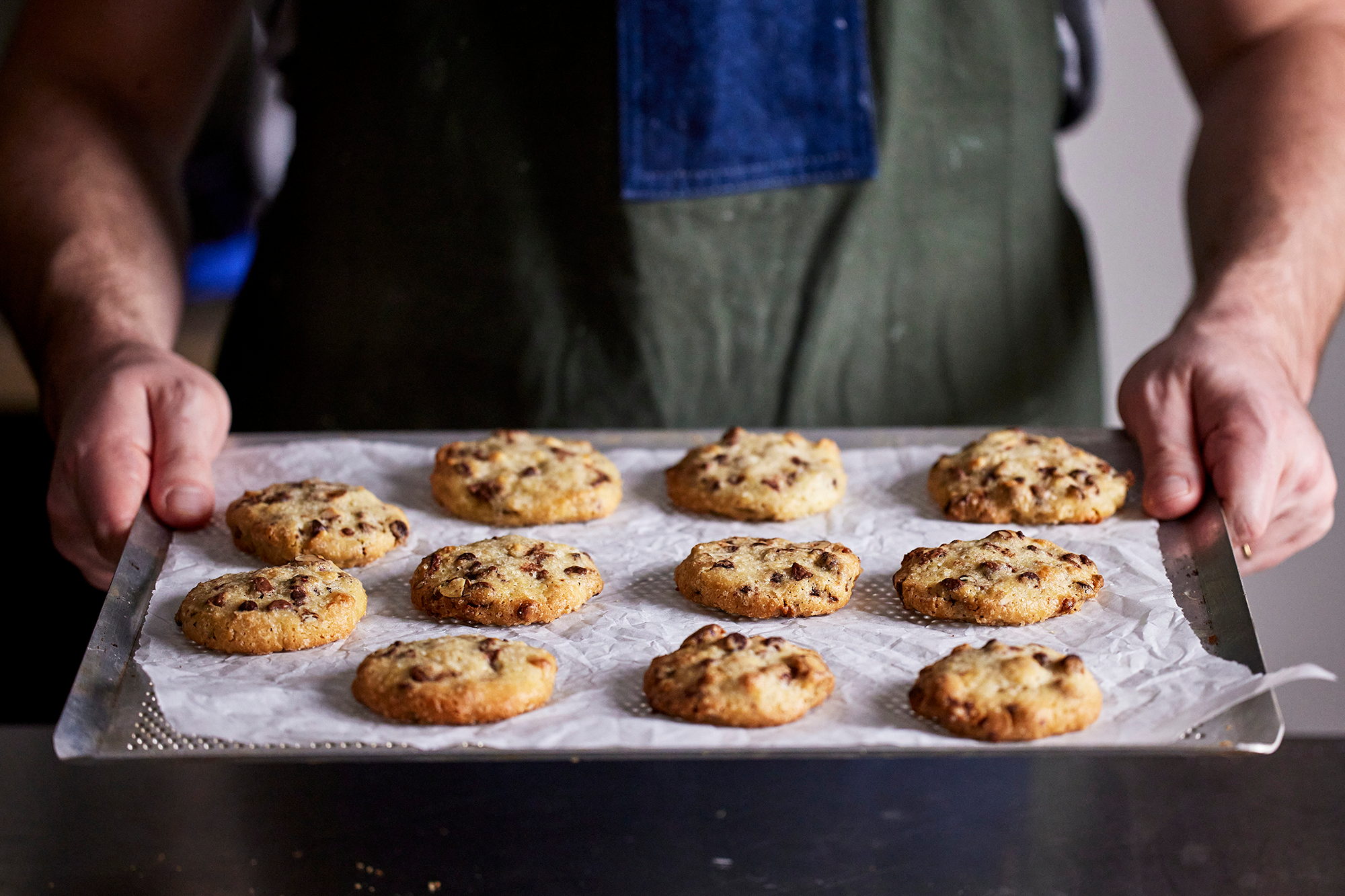 Mains présentant une plaque de cookies tout juste enfournés, tablier de travail
