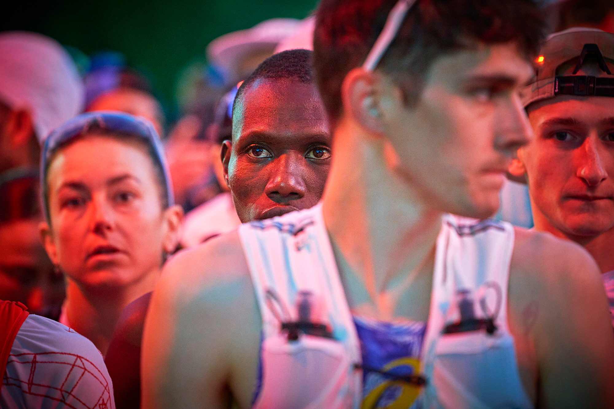 Visages tendus de coureurs serrés les uns contre les autres dans le sas, lumière rouge