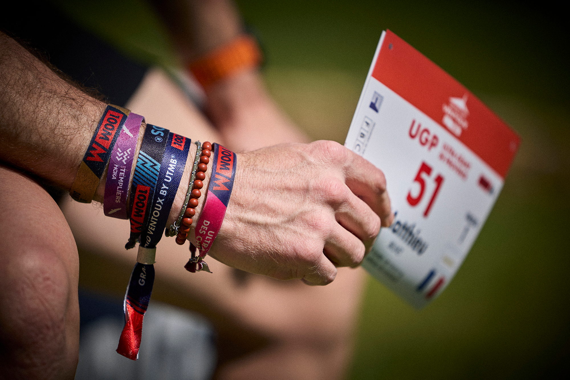 Main d'un coureur tenant son dossard, bracelets de course au poignet