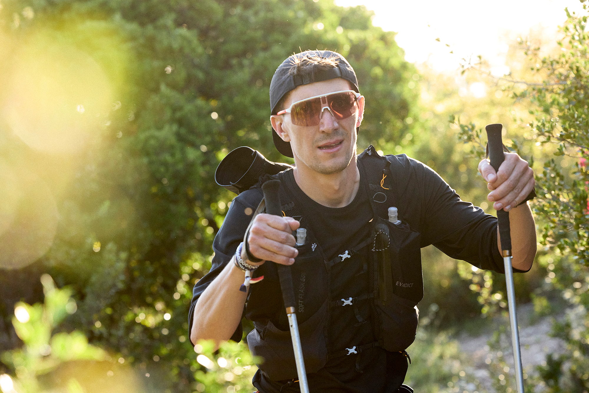 Coureur en contre-jour progressant bâtons en main dans la garrigue