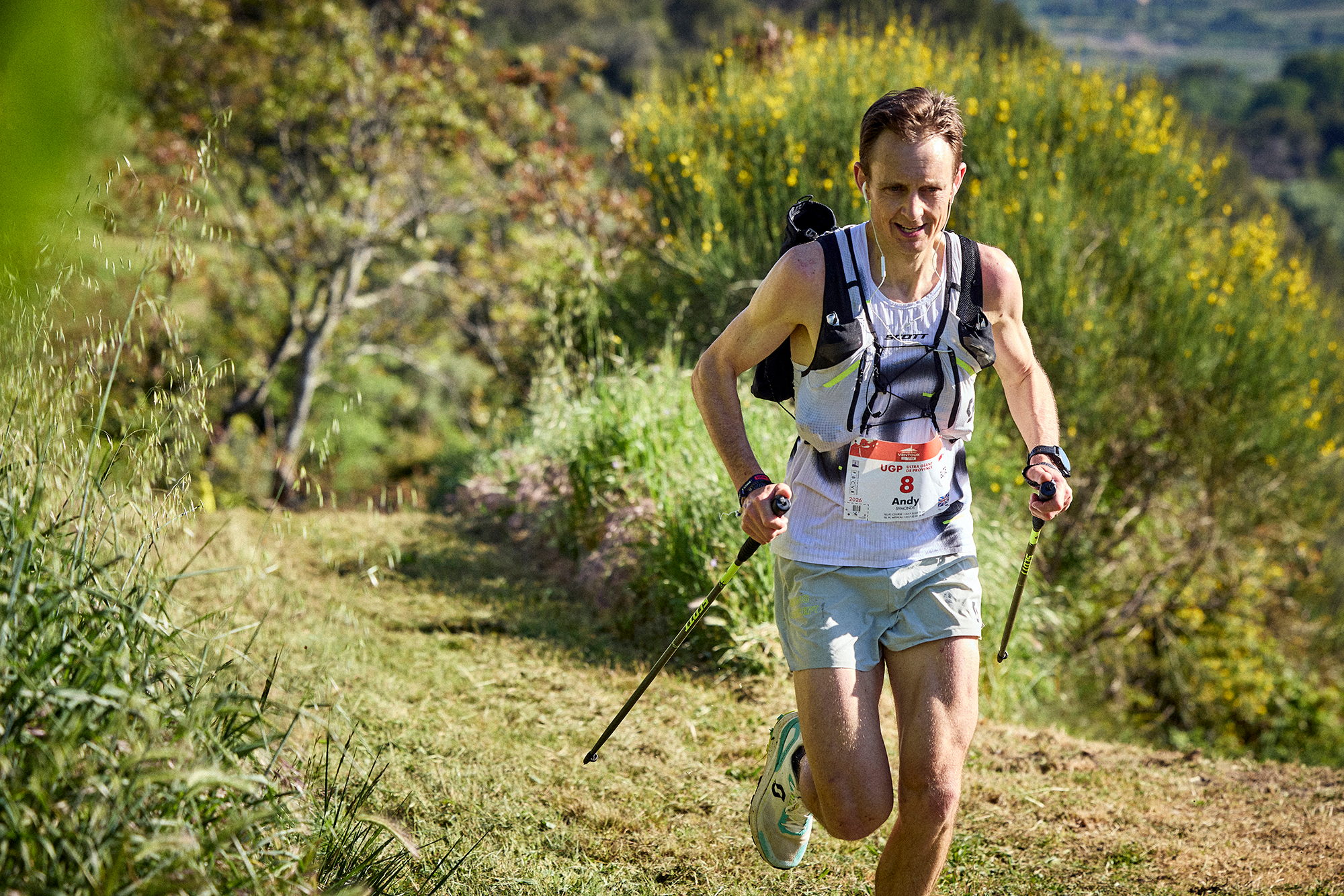 Coureur en montée sur un sentier herbeux, sac d'hydratation sur le dos