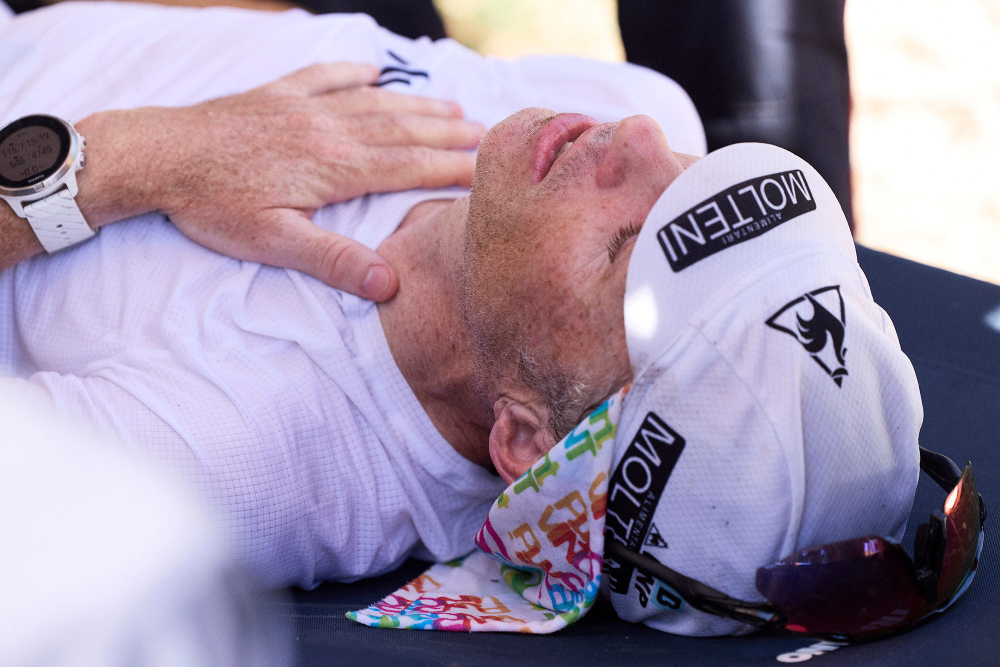 Coureur allongé sur le dos, yeux fermés, réconforté par un bénévole