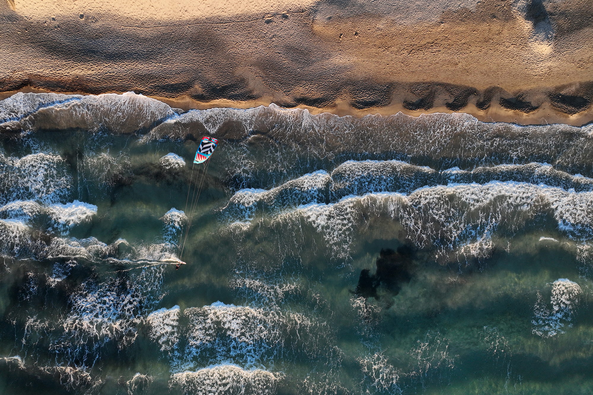 Vue aérienne des vagues déferlant en lignes parallèles sur une plage de sable