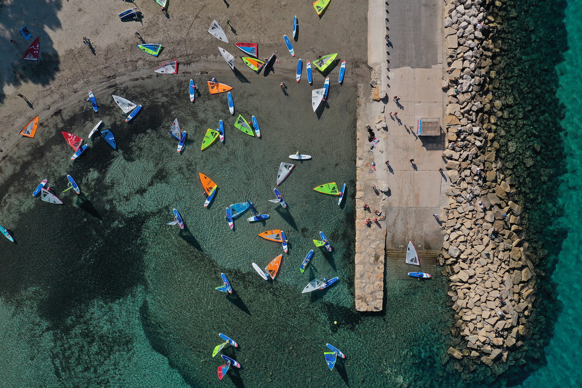 Vue aérienne de planches à voile aux voiles colorées le long d'une digue